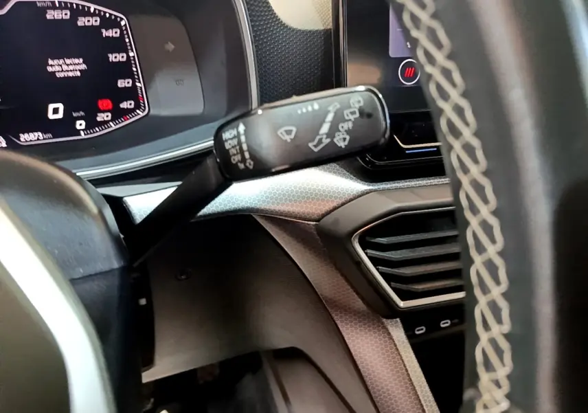 Gros plan sur le tableau de bord et le commodo d’essuie-glace d’une SEAT Leon gris foncé, affichage digital visible.