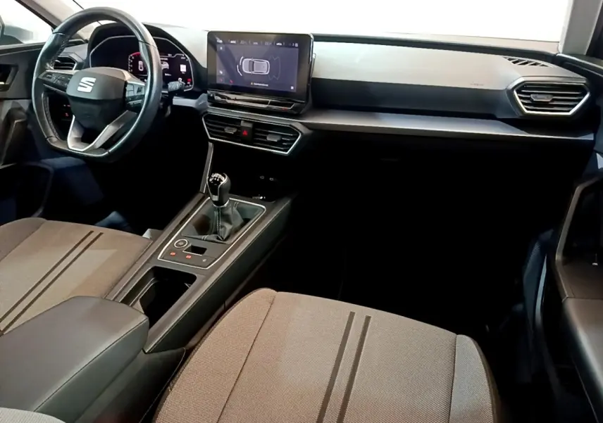 Intérieur SEAT Leon 2023 vu côté passager, tableau de bord noir avec écran tactile et levier de vitesse manuel.