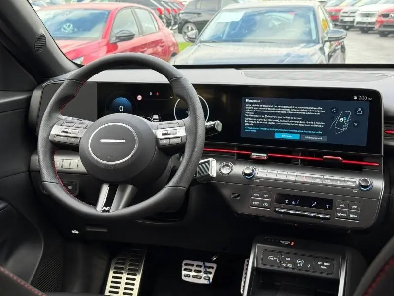 Vue intérieure du tableau de bord et volant cuir noir du Hyundai Kona 2025 avec écran tactile large et détails rouges.