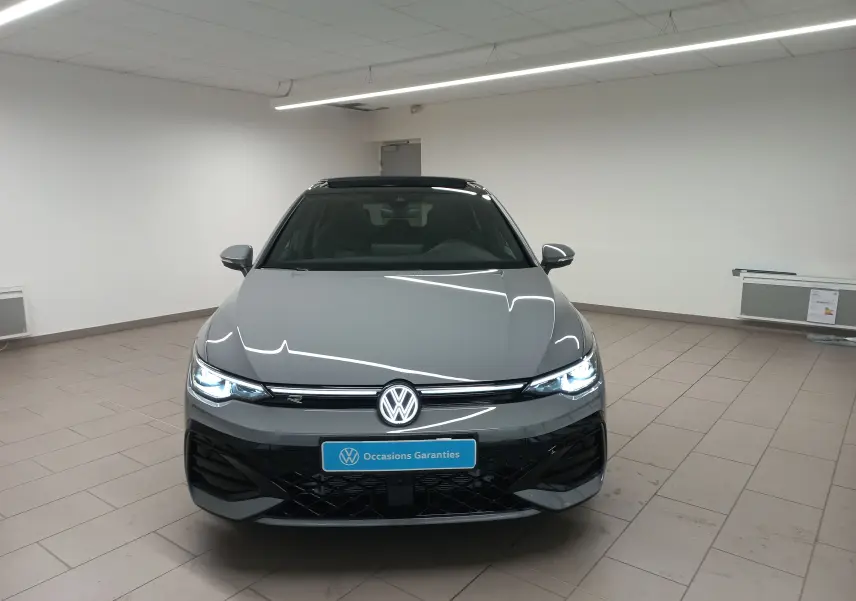 Vue avant d'une Volkswagen Golf 2.0 TDI R-Line gris lunaire avec phares allumés dans un showroom.