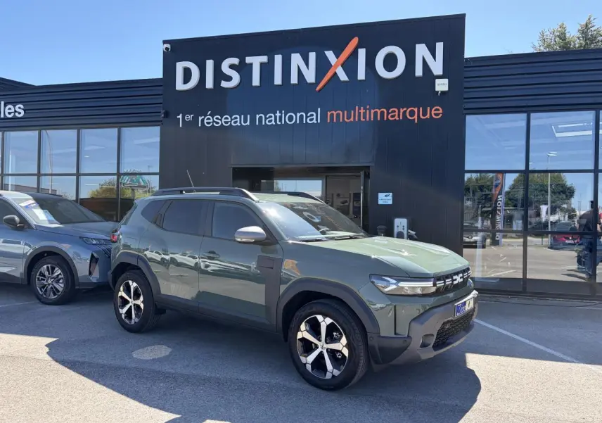 Vue 3/4 avant droite d'un Dacia Duster III hybride 2026 en kaki lichen avec jantes alliage diamantées devant un showroom Distinxion.