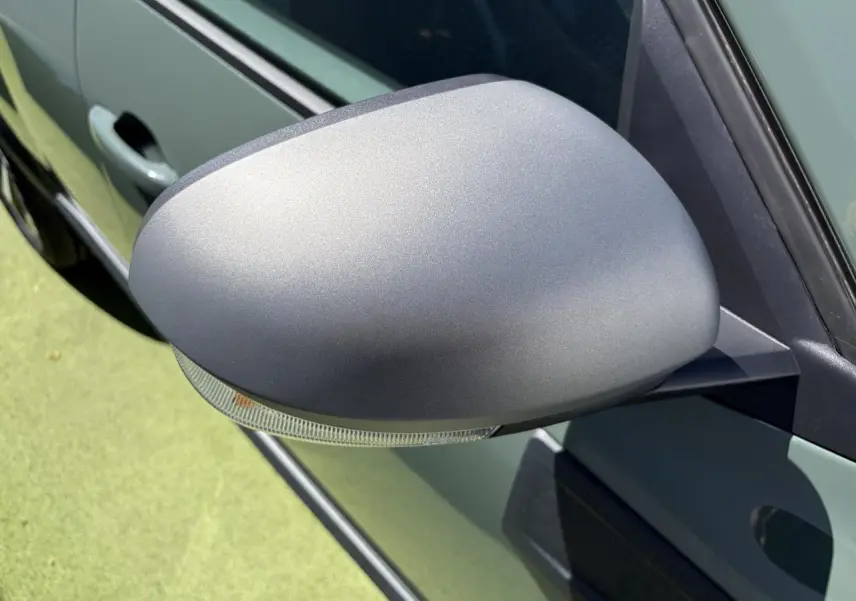 Gros plan sur le rétroviseur côté gauche gris mat du Dacia Duster III kaki lichen, avec clignotant intégré.