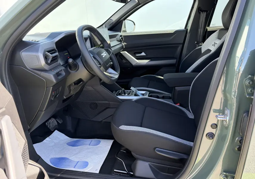 Vue intérieure côté conducteur du Dacia Duster III kaki lichen, montrant sièges noirs avec surpiqûres grises et tableau de bord moderne.