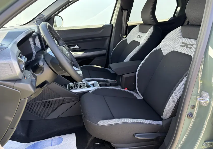 Vue intérieure côté conducteur du Dacia Duster III hybride, sièges bi-ton noirs et gris avec logo distinctif brodé.