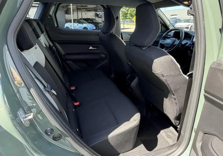 Vue intérieure arrière côté gauche du Dacia Duster III 2026 en kaki lichen, montrant les sièges noirs et l'avant du tableau de bord.