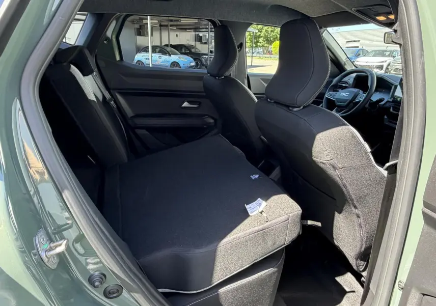 Vue intérieure arrière gauche du Dacia Duster III kaki lichen, banquette rabattue et sièges avant noirs visibles.