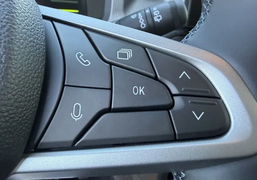 Gros plan sur les commandes multifonctions noires à droite du volant du Dacia Duster III kaki lichen, boutons de navigation et appel.