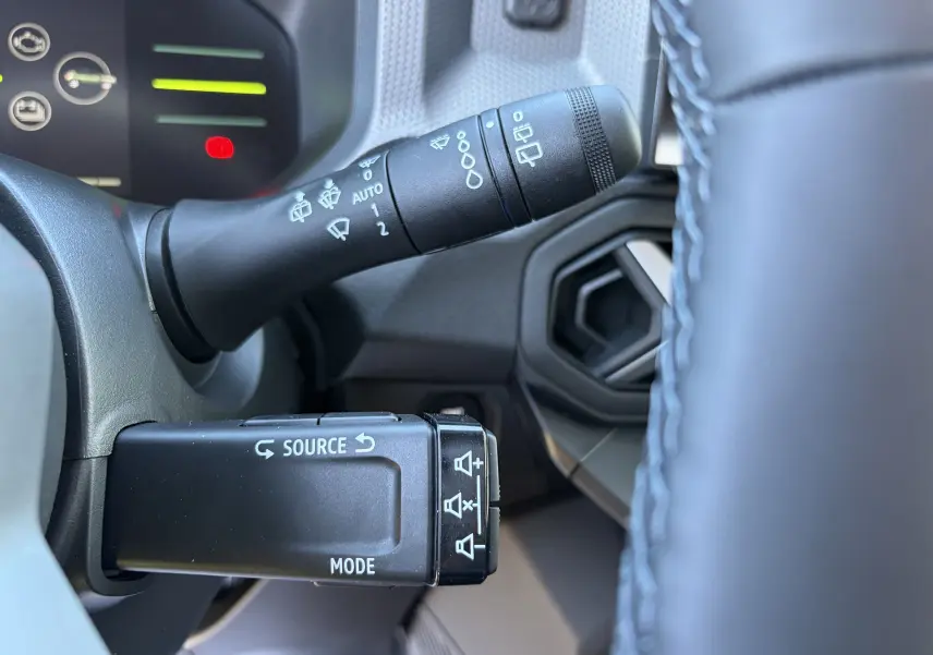 Gros plan sur les commandes au volant du Dacia Duster III hybride, avec détails des commandes de source et essuie-glace.