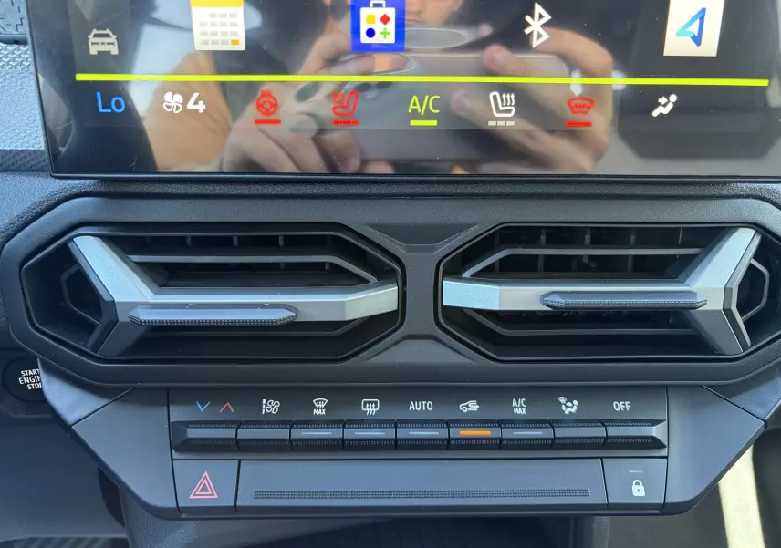 Vue rapprochée de la console centrale du Dacia Duster III 2026, montrant les aérateurs hexagonaux et les commandes de climatisation.