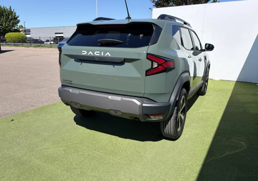 Vue 3/4 arrière droite du Dacia Duster III hybride en kaki lichen, avec barres de toit noires et jantes alliage 18 pouces.