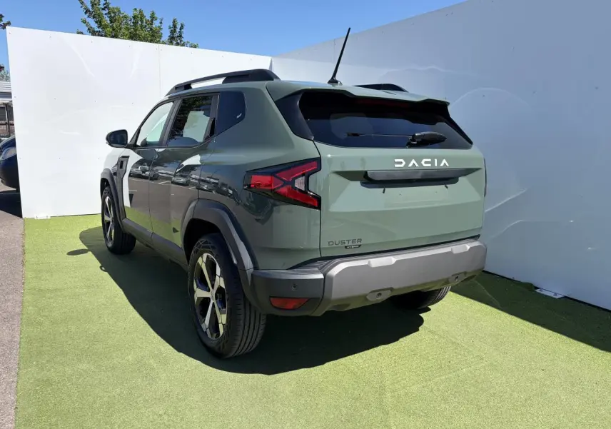 Vue 3/4 arrière droite du Dacia Duster III hybride en kaki lichen avec jantes alliage et barres de toit noires.