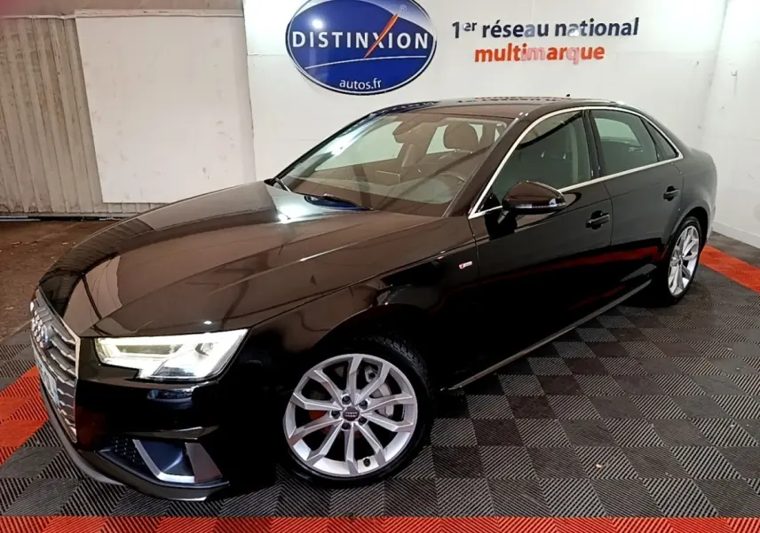 Audi A4 noire en 3/4 avant droit, avec jantes argentées et phares LED allumés en intérieur showroom.