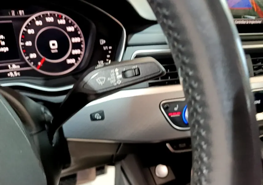 Gros plan sur le volant cuir et le tableau de bord numérique de l'Audi A4 noire, avec commandes de climatisation visibles.