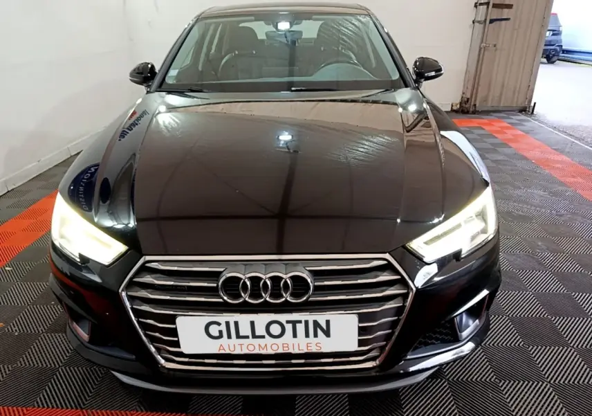 Vue avant d'une Audi A4 noire avec phares LED allumés et calandre chromée dans un garage.