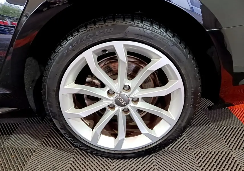 Gros plan sur la roue avant droite d’une Audi A4 noire 2018 avec jante en alliage argentée et logo Audi central.