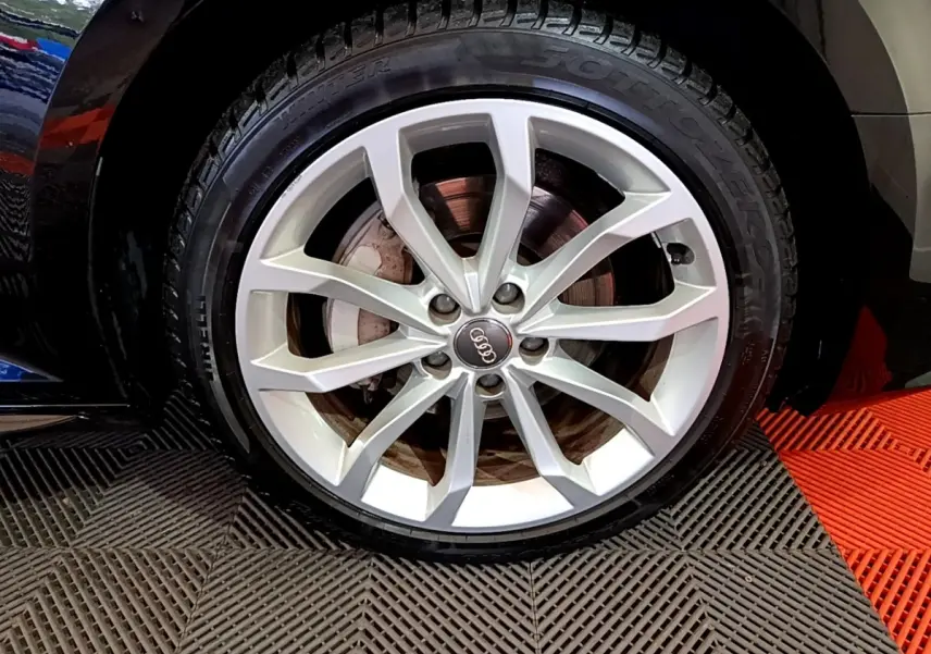 Gros plan sur la jante argentée et pneu Pirelli d'une Audi A4 noire, mettant en valeur le logo Audi central.