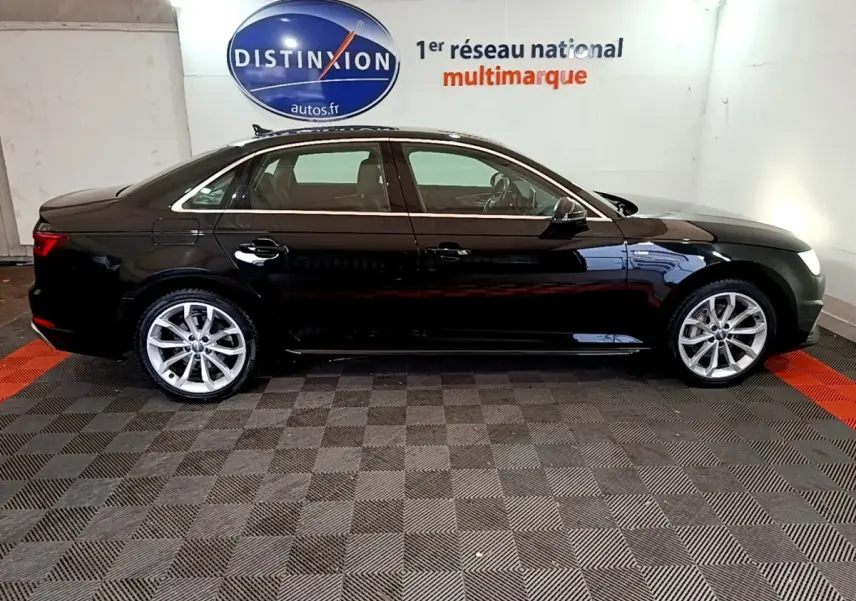 Audi A4 noire 2018 vue de profil côté gauche, stationnée en intérieur sur sol damier gris et rouge.