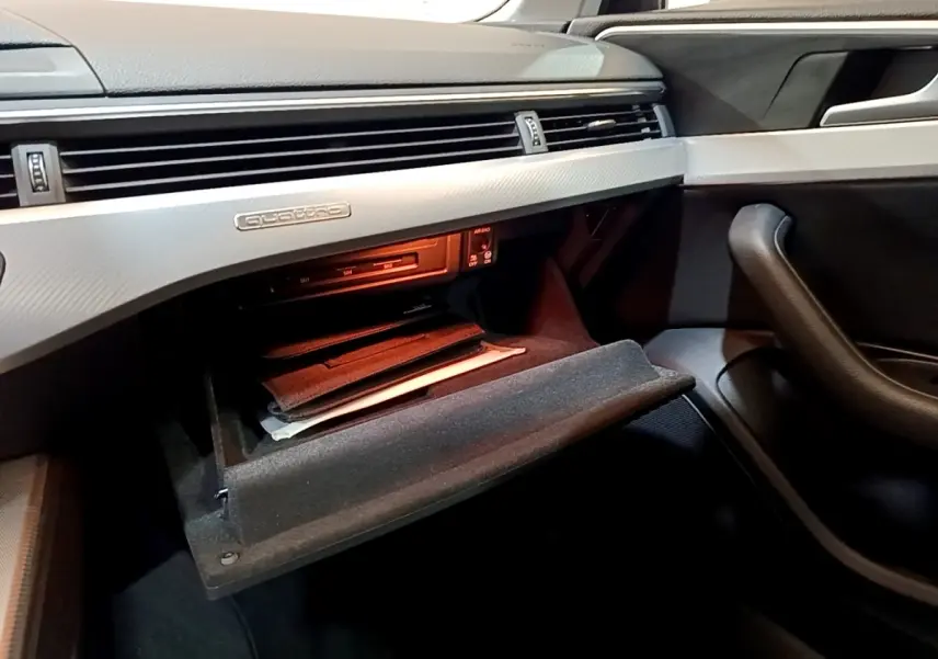 Intérieur côté passager de l'Audi A4 noire 2018, boîte à gants ouverte avec badge Quattro sur tableau de bord gris.