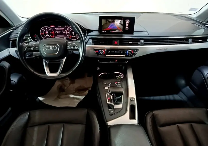 Vue intérieure avant de l'Audi A4 40 TDI noire, tableau de bord moderne avec écran tactile et volant cuir multifonctions.