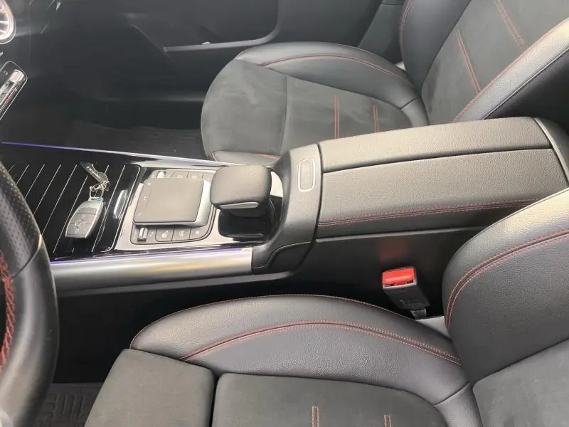 Vue intérieure rapprochée du tunnel central et des sièges noirs avec surpiqûres rouges d'une Mercedes GLA 200 d AMG Line.