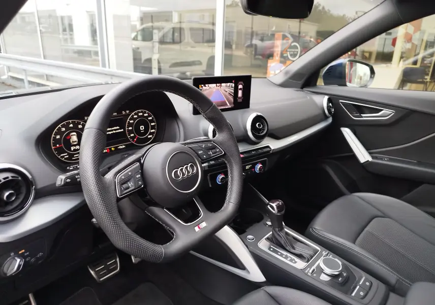 Vue intérieure côté conducteur de l'Audi Q2 35 TFSI 2023, avec volant sport, écran central et sellerie noire.