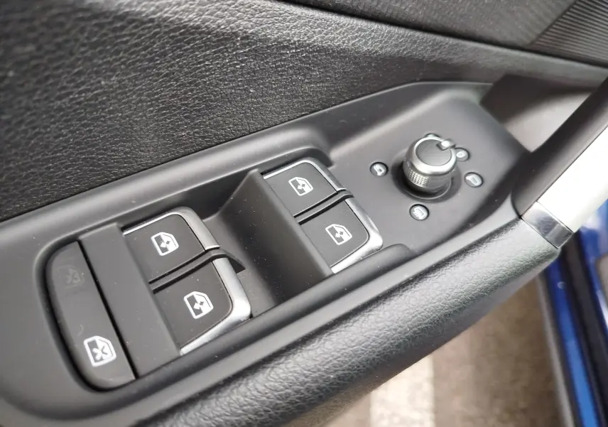 Gros plan sur les commandes de lève-vitres et réglage des rétroviseurs côté conducteur d’un Audi Q2 bleu Navarre 2023.