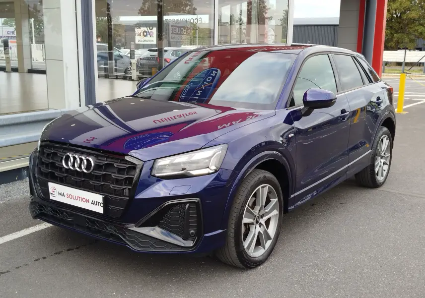Audi Q2 bleu Navarre en vue 3/4 avant droit, avec calandre noire S line et jantes alliage 18 pouces bicolores.
