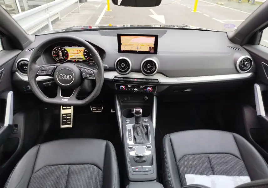 Vue intérieure frontale de l'Audi Q2 35 TFSI 2023 avec tableau de bord noir, volant sport et écran central GPS.