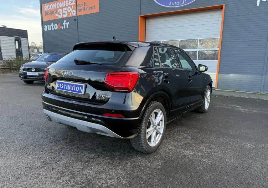 Audi Q2 noir brillant vue 3/4 arrière droit, avec badge 30 TDI et jantes alliage visibles sur un parking extérieur.
