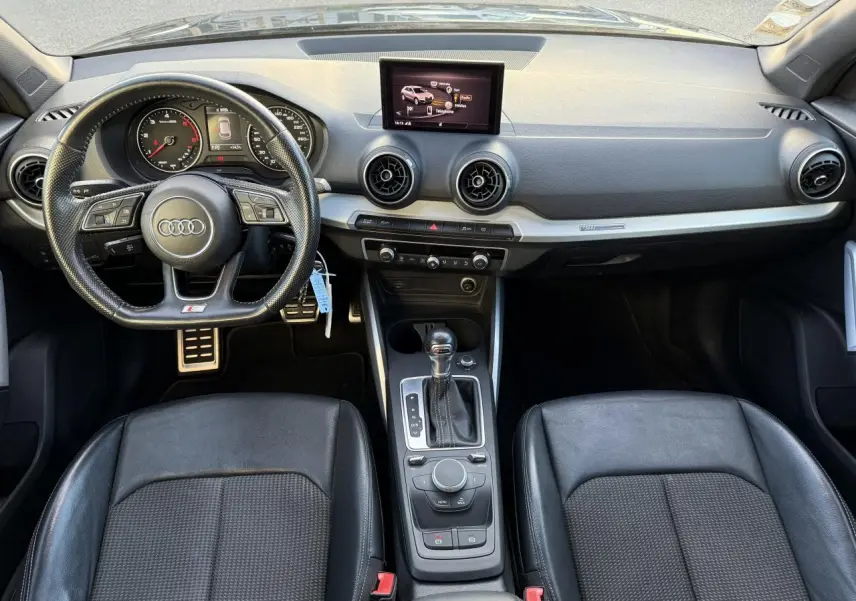 Vue intérieure avant de l'Audi Q2 S Line 2019 avec volant cuir multifonction noir et console centrale avec boîte auto.