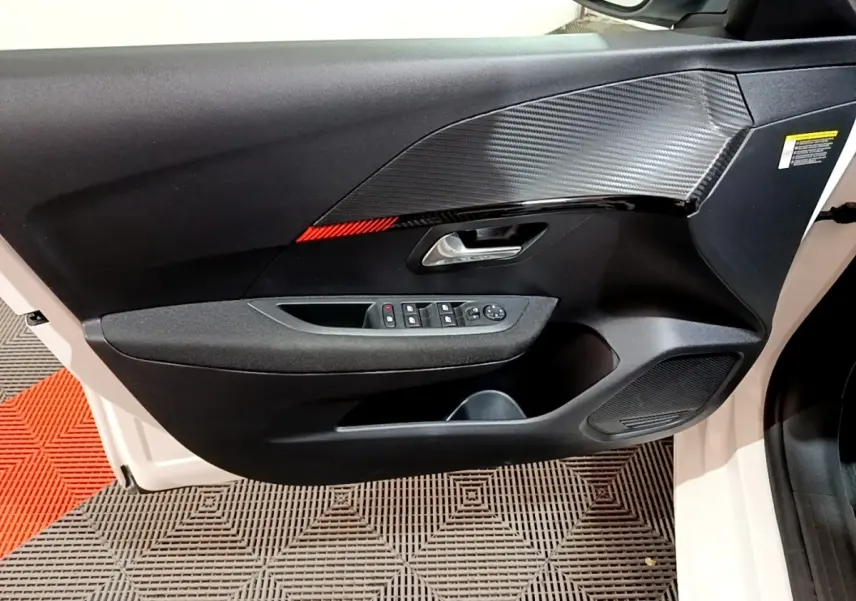 Vue côté gauche de la porte intérieure noire avec insert décoratif carbone et bande rouge sur Peugeot 208 blanc électrique.