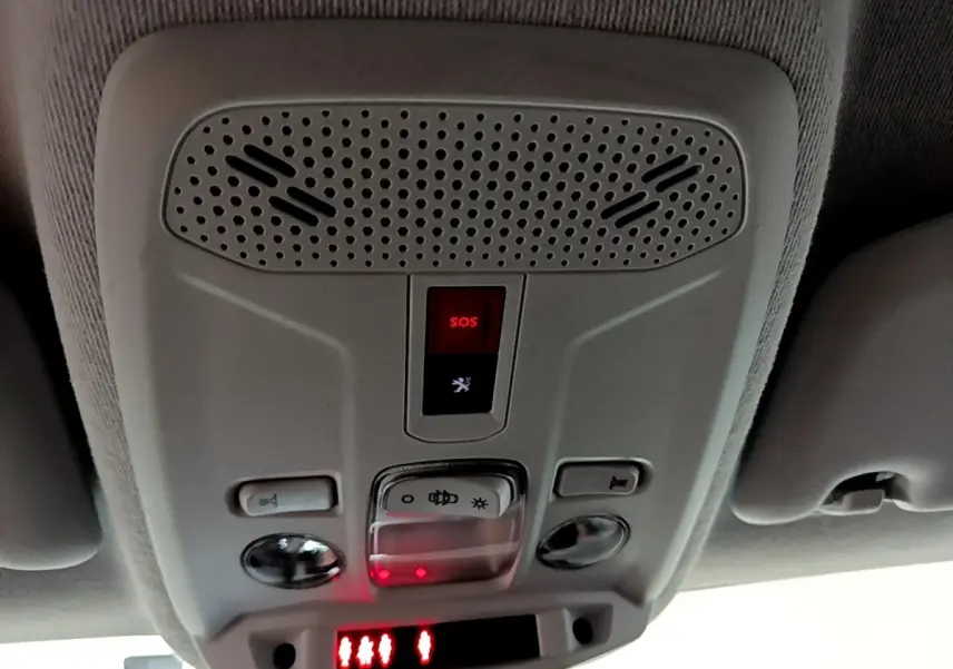 Vue en gros plan du panneau de commande au plafond intérieur gris clair du Peugeot 208 électrique, avec bouton SOS rouge éclairé.