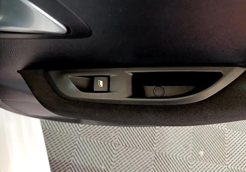 Bouton de commande de vitre sur la porte côté gauche intérieure d'une Peugeot 208 Electrique Active Business blanche.