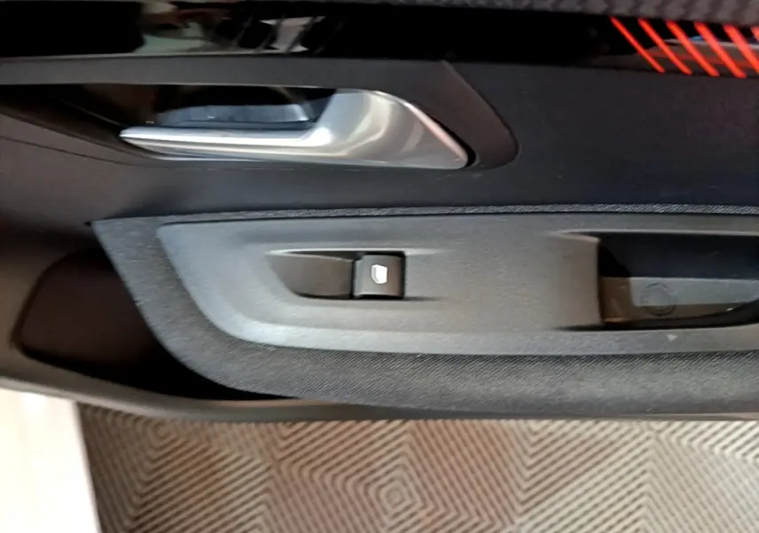 Détail de la poignée intérieure et commande de lève-vitre côté gauche d'une Peugeot 208 électrique blanche.
