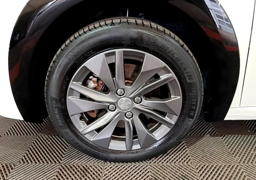 Gros plan sur la roue avant droite d'une Peugeot 208 électrique blanche, avec jante alliage gris et pneu Michelin.