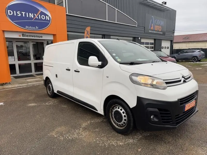 Vue 3/4 avant droit d'un Citroën Jumpy blanc Banquise avec jantes tôle et calandre noire, stationné devant un garage.