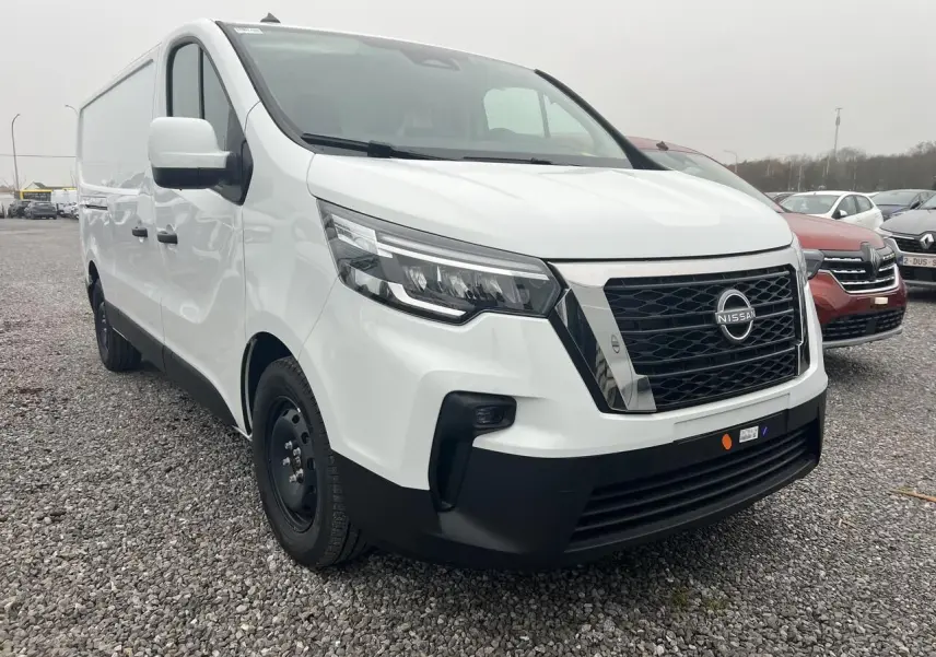 Vue 3/4 avant d’un utilitaire Nissan Primastar blanc avec calandre noire et jantes tôles noires sur un sol gravillonné.