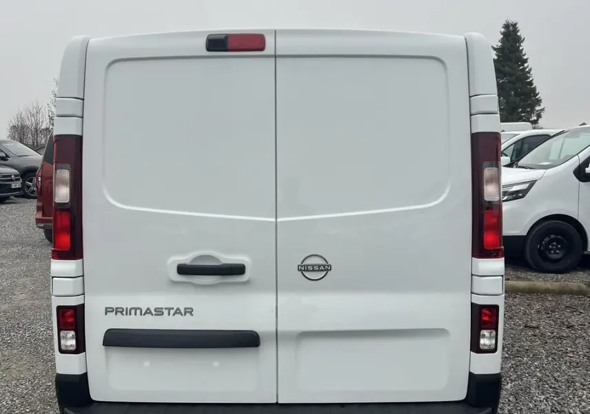 Vue arrière d’un utilitaire Nissan Primastar blanc avec portes battantes et feux arrière verticaux.