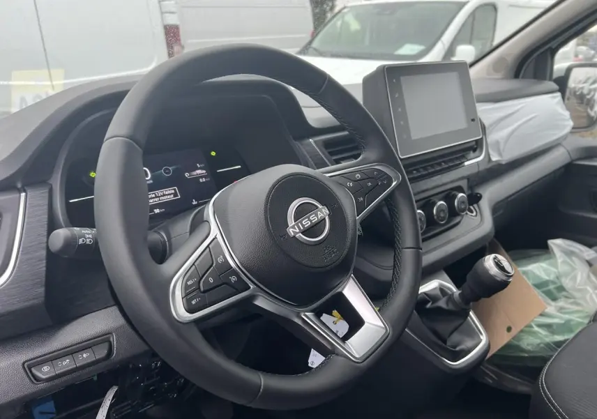 Vue intérieure côté conducteur du Nissan Primastar blanc 2025, volant multifonction et écran tactile central visible.