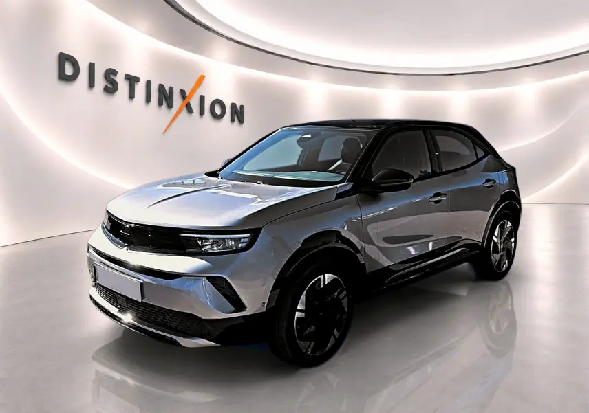 Opel Mokka Electric gris en 3/4 avant droit, toit noir et jantes alu distinctives dans un showroom lumineux.