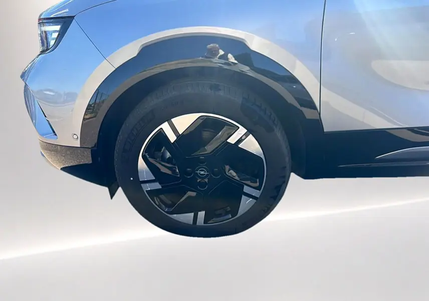 Gros plan sur la roue avant gauche et la partie basse grise d’un Opel Mokka Electric 156 gs avec jante alu noire et argent.