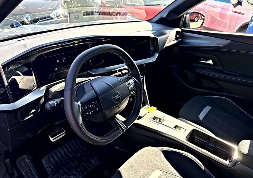 Vue intérieure côté conducteur de l'Opel Mokka Electric gris, volant multifonction et tableau de bord numérique moderne.