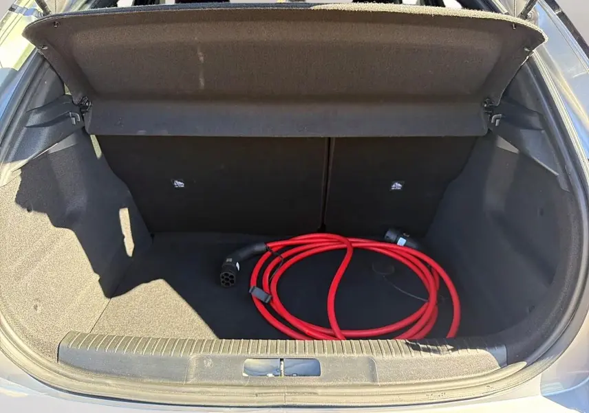 Coffre ouvert d’un Opel Mokka Electric gris, montrant un câble de recharge électrique rouge enroulé.