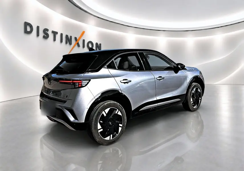 Opel Mokka Electric gris en 3/4 arrière droit, toit noir et jantes alu distinctives dans un showroom lumineux.
