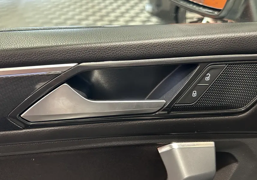 Poignée intérieure côté gauche en métal brossé avec commandes de verrouillage sur la portière noire du Volkswagen Tiguan Allspace blanc.