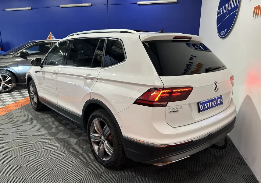 Volkswagen Tiguan Allspace blanc vu en 3/4 arrière droit, avec feux arrière allumés et jantes alliage visibles.