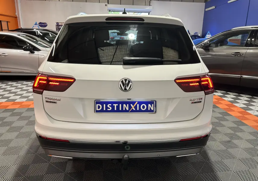 Vue arrière d'un Volkswagen Tiguan Allspace blanc avec feux LED allumés et attelage dans un showroom.