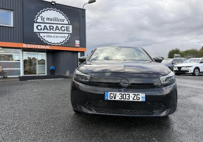 Opel Corsa noire vue de face, calandre Vizor et plaque d'immatriculation française visible devant un garage.