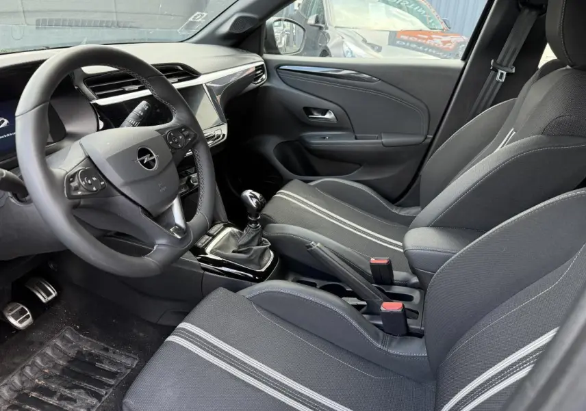 Intérieur avant droit de l'Opel Corsa noir 2024 avec sièges sport tissu noir et blanc et volant multifonction.