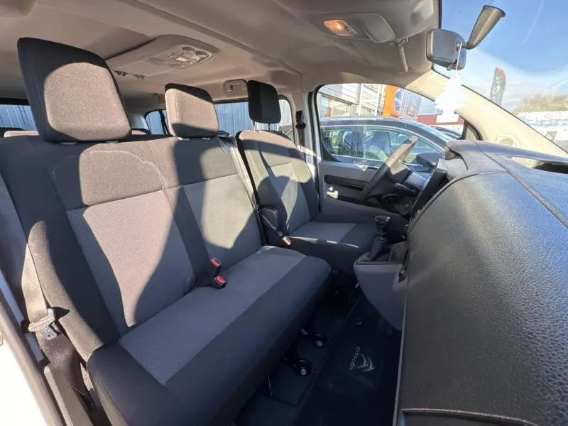 Vue intérieure côté conducteur du Citroën Jumpy XL blanc, montrant les sièges tissu Mica et tableau de bord noir.